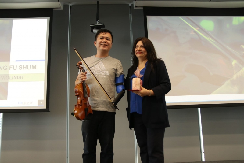 man with prosthetic arm holds violin next to woman holding award
