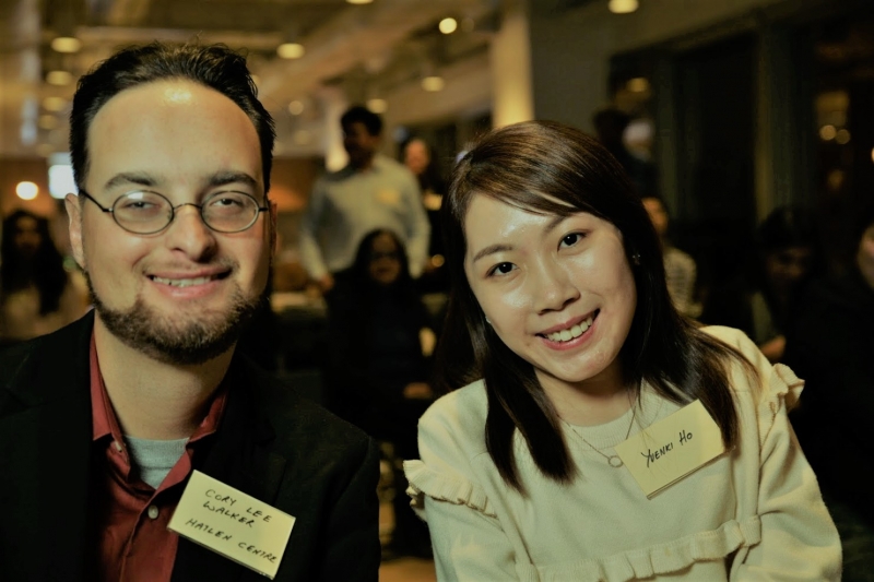 A man with glasses and woman in a white smock smile at the camera sitting next to each other 