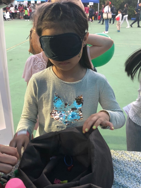 A girl is wearing a blindfold while trying to pick a prize from a bag.