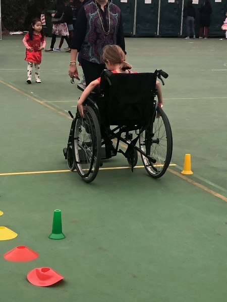 The back of a girl can be seen as she is sitting in a wheelchair attempting the wheelchair race.