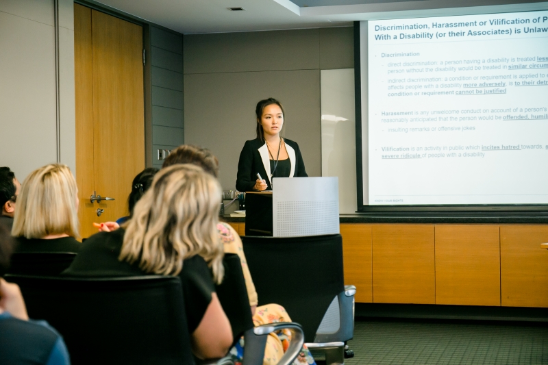 A female Skadden staff member in business attire is giving a presentation whilst standing behind a podium