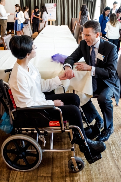 A man in a suit sitting whilst speaking with a wheelchair-bound woman.