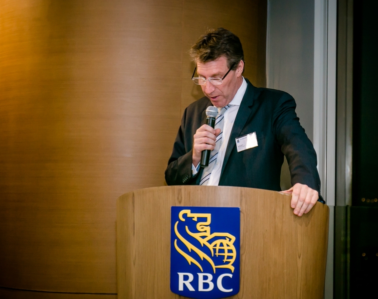 A male Royal Bank of Canada staff member in a suit is giving a speech whilst standing behind a podium