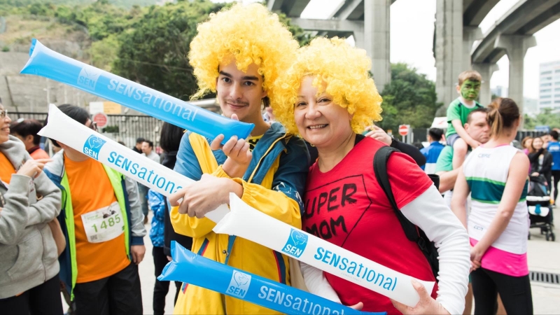 two people wearing yellow and blue wigs and holding sensational consultancy balloons pose